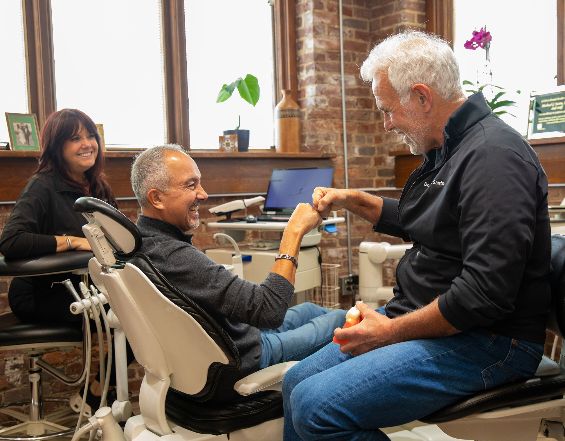 A hygienist is next to a smiling patient who is sitting in a dental office chair