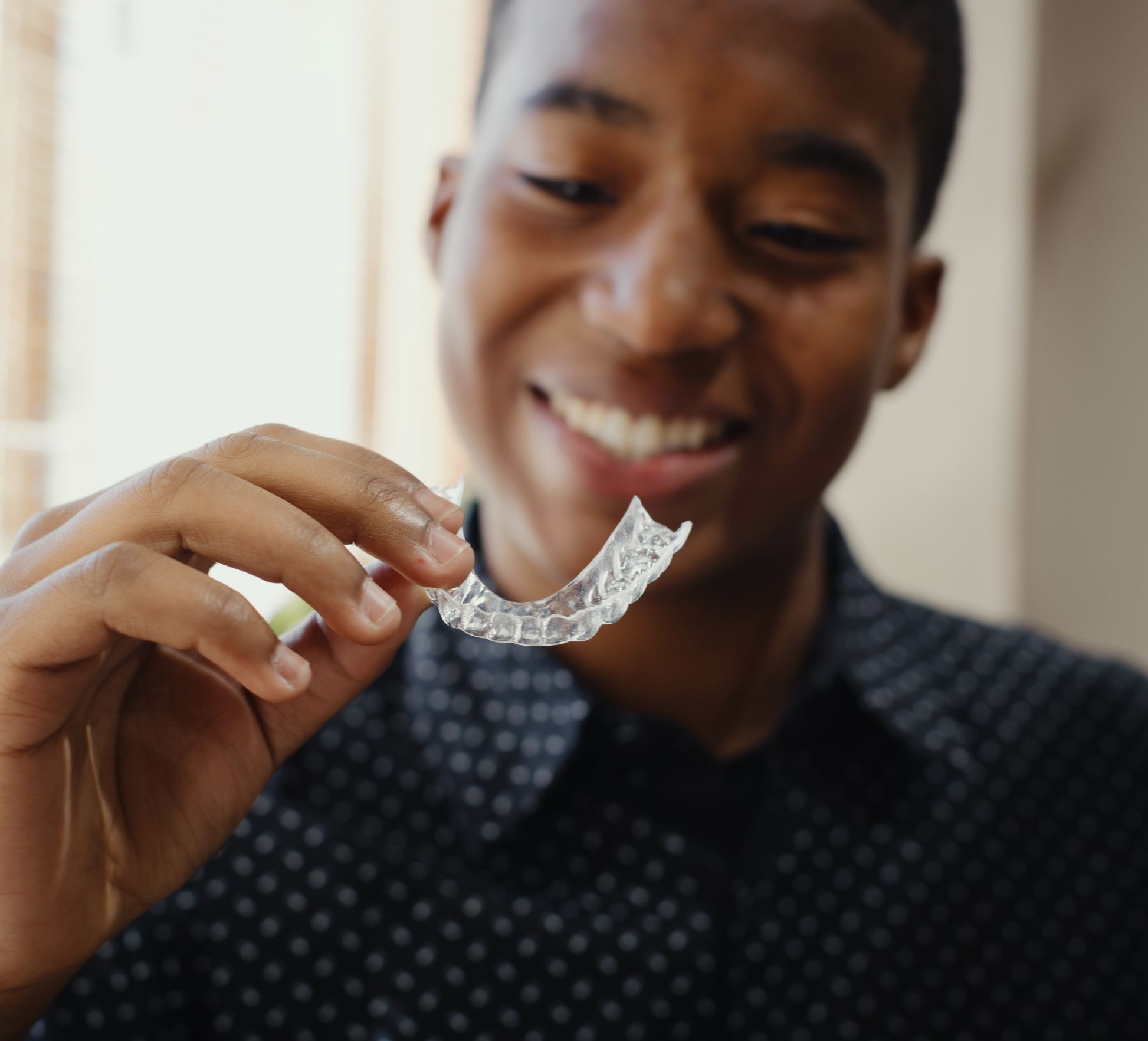 A smiling teenage boy looks at his Invisalign aligner